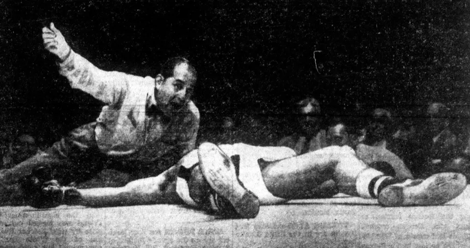 Referee Ruby Goldstein counting over a fallen boxer in the ring